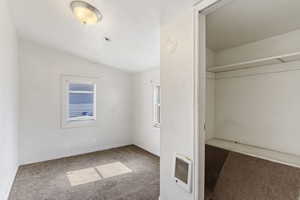 Unfurnished bedroom featuring vaulted ceiling, heating unit, carpet, and baseboards