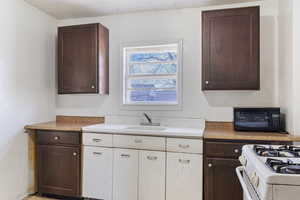 Kitchen with white range with gas stovetop, a sink, light countertops, dark brown cabinets, and white cabinetry