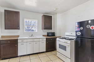 Kitchen featuring light tile patterned floors, a sink, black appliances, light countertops, and dark brown cabinets