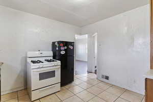 Kitchen featuring visible vents, light countertops, white gas range oven, freestanding refrigerator, and light tile patterned flooring