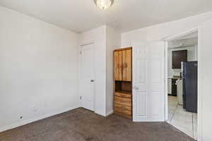 Unfurnished bedroom featuring baseboards, light carpet, a textured ceiling, and freestanding refrigerator