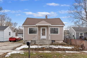 Bungalow-style home featuring aphalt driveway, a chimney, roof with shingles, and fence