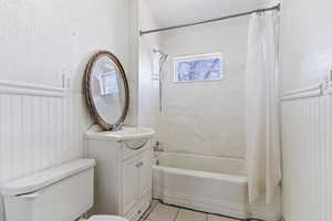 Bathroom with tile patterned floors, shower / bath combo with shower curtain, toilet, wainscoting, and vanity