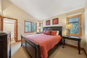 Bedroom featuring lofted ceiling, baseboards, connected bathroom, and light colored carpet