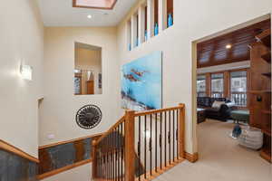 Hallway featuring a skylight, recessed lighting, a towering ceiling, carpet flooring, and an upstairs landing