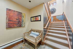 Staircase featuring stone finish flooring, a baseboard heating unit, and baseboards