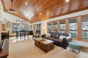 Carpeted living area featuring vaulted ceiling, a ceiling fan, wood ceiling, and baseboards