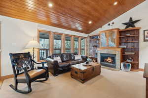 Living room featuring a fireplace, carpet flooring, wood ceiling, baseboards, and vaulted ceiling