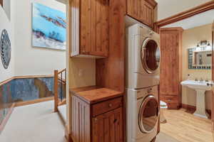 Laundry area featuring stacked washer and dryer, light wood-style flooring, and baseboards