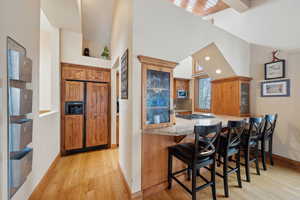 Bar featuring tasteful backsplash, baseboards, a high ceiling, light wood-style floors, and stainless steel gas stovetop