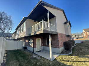 Back of property featuring a covered patio, covered balcony, brick siding, lawn and fence