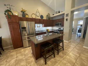 Kitchen featuring high vaulted ceiling, a breakfast bar, sink, stainless steel appliances, and large center island