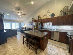 Kitchen with light tile floors, stainless steel refrigerator with ice dispenser, a vaulted textured ceiling, a kitchen bar, and open floor plan