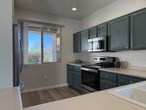 Kitchen featuring a sink, dark wood finished floors, appliances with stainless steel finishes, light countertops, and baseboards