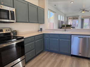 Kitchen featuring light wood finished floors, a sink, stainless steel appliances, light countertops, and ceiling fan