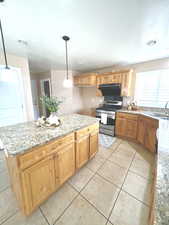 Kitchen featuring stainless steel gas range oven, light stone countertops, range hood, and a sink