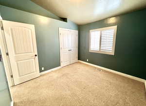Unfurnished bedroom featuring visible vents, baseboards, carpet, lofted ceiling, and a closet