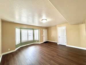 Empty room featuring dark wood finished floors, baseboards, visible vents, and a textured ceiling