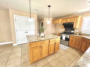 Kitchen featuring light stone countertops, pendant lighting, light tile patterned flooring, a textured ceiling, and stainless steel gas range