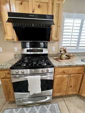 Kitchen featuring range hood, light stone counters, light tile patterned flooring, and gas stove