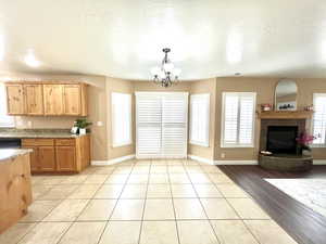 Kitchen featuring light stone countertops, an inviting chandelier, light tile patterned flooring, a fireplace with raised hearth, and hanging light fixtures