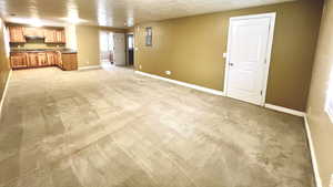 Unfurnished living room featuring electric panel, baseboards, and light carpet