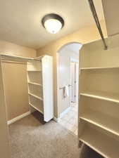 Walk in closet featuring light carpet, light tile patterned floors, and arched walkways