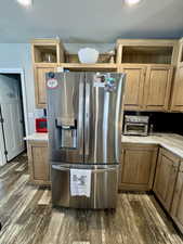 Kitchen featuring light countertops, stainless steel refrigerator with ice dispenser, open shelves, a toaster, and dark wood-style flooring