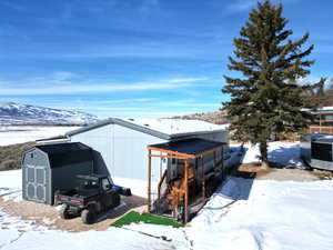 Snow covered structure with a mountain view, a storage shed, an outdoor structure, a pole building, and a carport