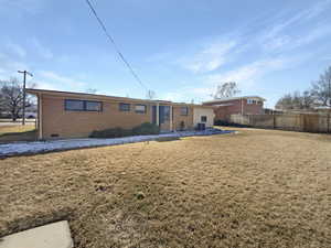 Rear view of house with a yard, fence, brick siding, and crawl space