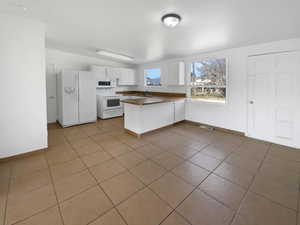 Kitchen with a sink, dark countertops, white cabinetry, white appliances, and a peninsula