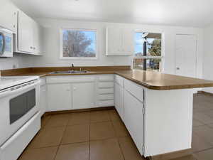 Kitchen with white appliances, light tile patterned flooring, a peninsula, and a sink