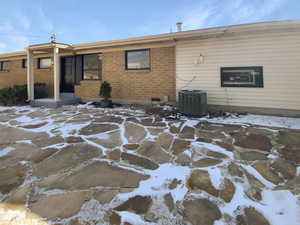 Snow covered back of property with brick siding and central air condition unit