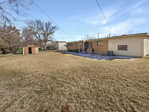 Rear view of property featuring an outbuilding, a storage unit, central air condition unit, a lawn, and brick siding