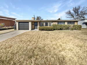 Ranch-style house with driveway, a front yard, a garage, brick siding, and a chimney