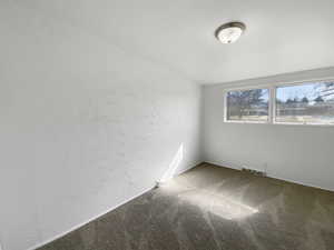 Empty room with visible vents, carpet, and a textured wall