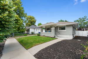 View of front of home with brick siding, a shingled roof, fence, a gate, and a front lawn