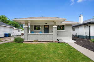 View of front facade featuring a shingled roof, covered porch, central air condition unit, a front lawn, and brick siding