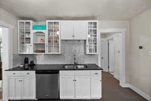 Kitchen with a sink, white cabinetry, baseboards, stainless steel dishwasher, and backsplash