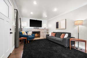 Living room featuring a stone fireplace, recessed lighting, baseboards, dark wood-style floors, and crown molding