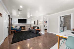 Living area featuring crown molding, visible vents, dark wood finished floors, and a fireplace