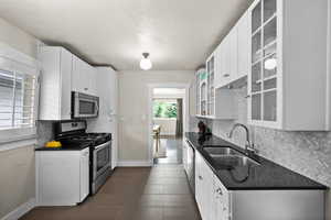 Kitchen featuring decorative backsplash, dark countertops, appliances with stainless steel finishes, white cabinetry, and a sink