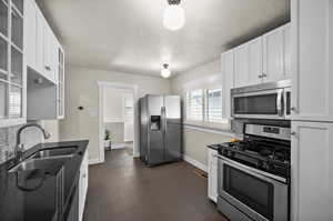 Kitchen with white cabinets, glass insert cabinets, a sink, stainless steel appliances, and backsplash