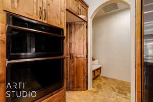 Kitchen with multiple ovens, stone finish floor, arched walkways, and wood cabinetry