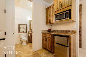 Casita kitchenette & bathroom featuring vanity, toilet, sink, fridge, microwave, and stone tile flooring