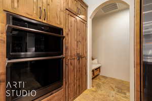 Kitchen featuring wood cabinetry, arched walkways, stone finish floor, and stainless steel appliances