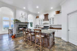 Kitchen featuring a multi sided fireplace, a breakfast bar area, stainless steel gas stove, premium range hood, and glass insert cabinets
