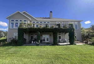 Back of house featuring a lawn, a deck, a patio, french doors, and a chimney