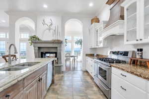 Kitchen featuring light stone countertops, a sink, a fireplace, stainless steel appliances, and custom range hood