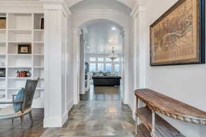 Hall with arched walkways, baseboards, an inviting chandelier, ornamental molding, and ornate columns
